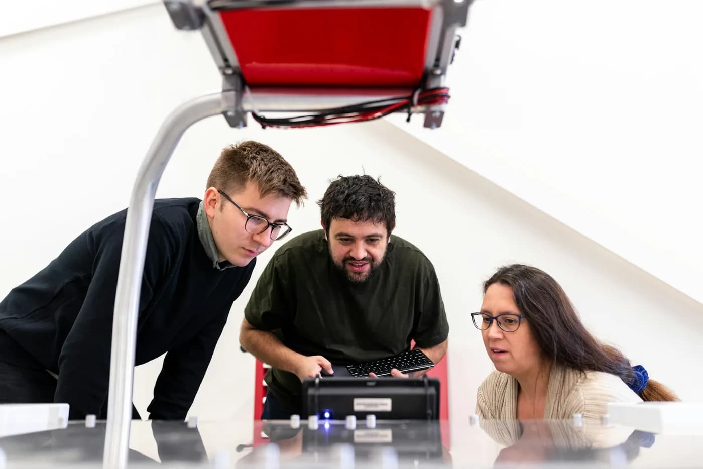Drei Menschen beugen sich über eine Maschine, die sie gemeinsam testen